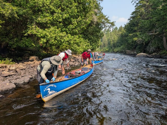 A group launching canoes into a river from a rocky bank with forest on both sides