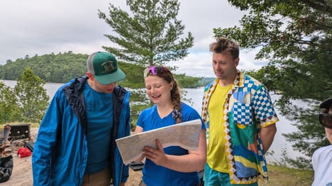 Three people on a rock above a lake, one holding an open topographic map while the others lean in to look at it