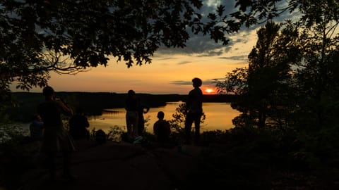 A group standing on a rock lookout at sunset with lake and forest below